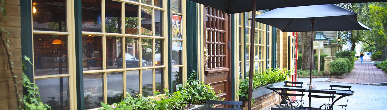 Cozy and picturesque street cafe  (bistro) with window boxes, chairs, tables and umbrellas. Brick sidewalk, French windows and front door. City life; cafe society; small restaurant; Savannah, Georgia.
