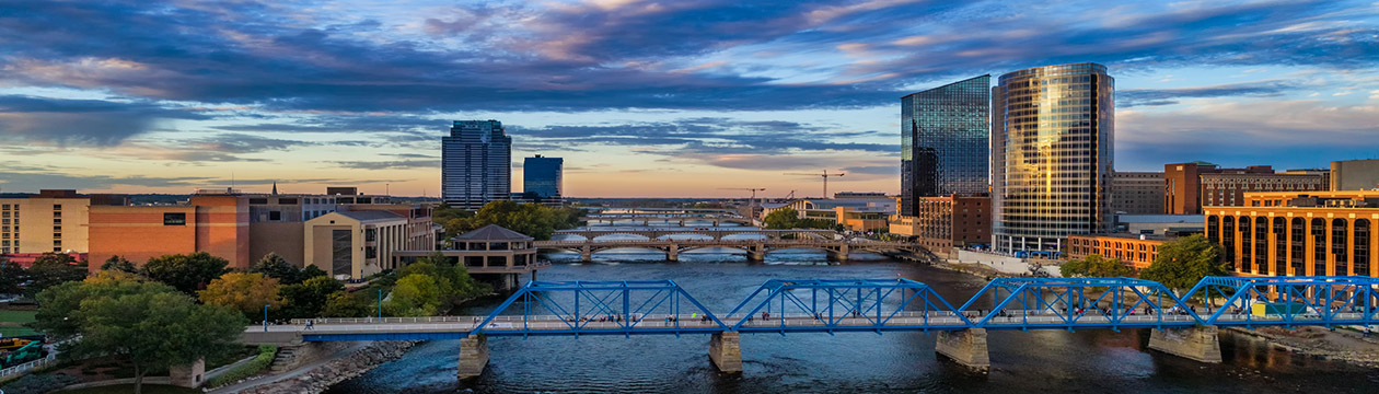 Downtown Grand Rapids aerial with Grand River and bridges during sunset, with a beautiful cloudscape in the background, and the Blue Bridge pedestrian bridge in the foreground.